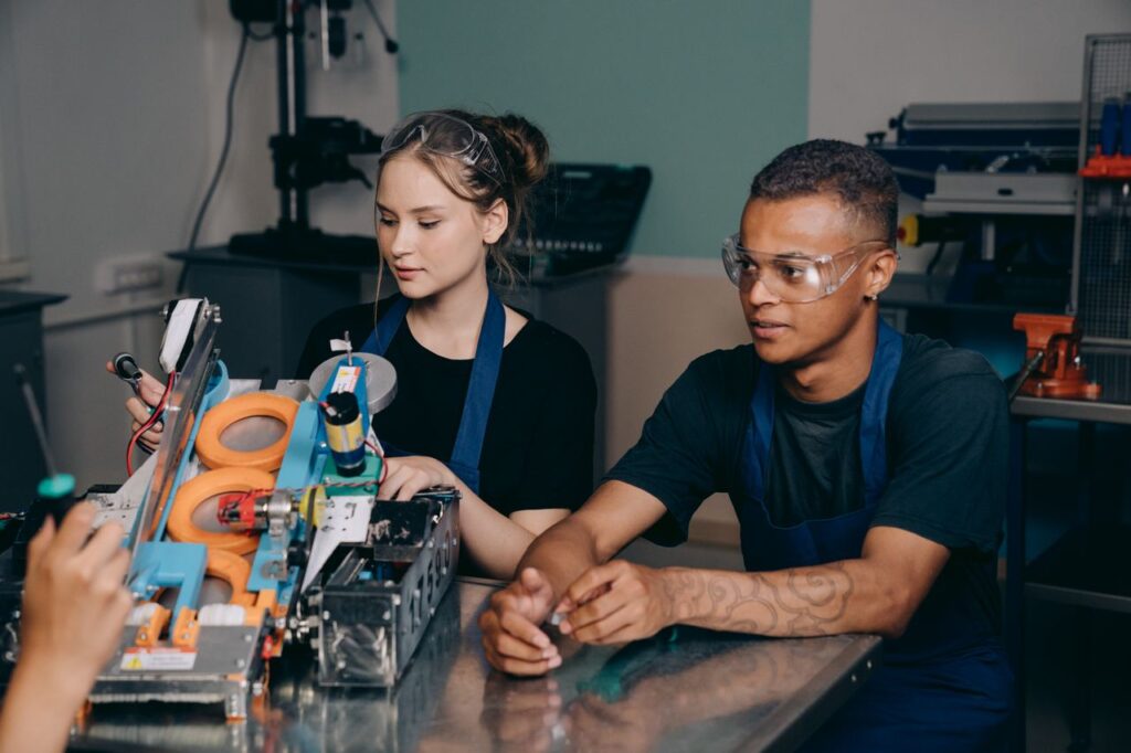 Two young engineers collaborating on a complex machine in an industrial setting.